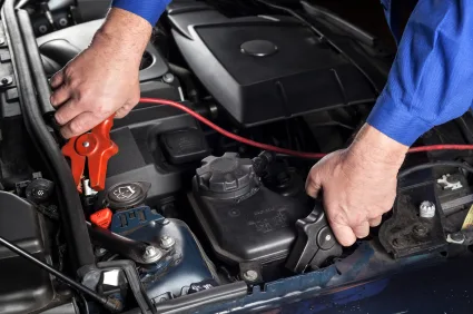 A mechanic is jump-starting a car with a booster cable Towing in Eugene - A mechanic is jump-starting a car with a booster cable